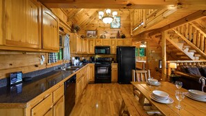 A wooden cabin interior with a kitchen, dining area, and staircase. - Free Attractions | Secluded, New Hot Tub w/ Views, Fireplace, Pet-Friendly (Gatlinburg)