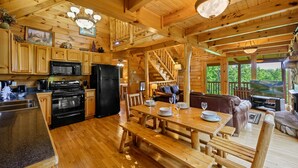 A wooden cabin interior with a kitchen, dining area, and a staircase leading to a loft. - Free Attractions | Secluded, New Hot Tub w/ Views, Fireplace, Pet-Friendly (Gatlinburg)