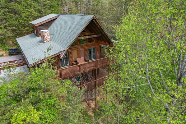 A cabin with a green roof, wooden exterior, and a balcony. - Free Attraction Passes | Firepit, Theater, Pool Table, Hot Tub, Private (Sevierville)