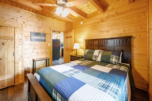A wooden cabin bedroom with a bed, nightstand, and a ceiling fan. - Free Attraction Passes | Firepit, Theater, Pool Table, Hot Tub, Private (Sevierville)