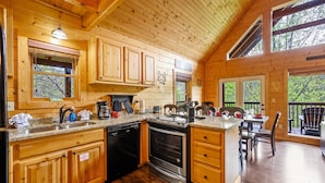 A wooden cabin kitchen with a built-in oven, a sink, and a dining area with a table and chairs. - Free Attraction Passes | Firepit, Theater, Pool Table, Hot Tub, Private (Sevierville)