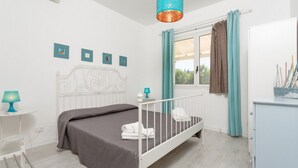 Ein Schlafzimmer mit Bett, Schreibtisch, Stuhl, einem Fenster mit Vorhängen und einer Pendelleuchte.