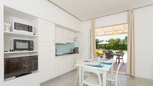 Eine moderne Küche mit weißen Schränken, einer Mikrowelle und einem eingebauten Backofen. Es gibt eine Essecke mit einem Tisch für zwei Personen und einen Blick auf eine Außenpatio mit Pool und Sonnenschirmen.