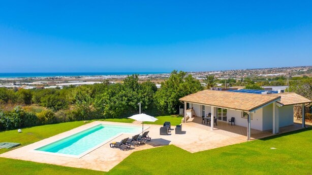 Ein Haus mit Swimmingpool, Sitzgelegenheiten im Freien und Meerblick.