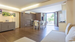 A modern living room with a sofa, a dining area with a table and chairs, and a kitchen visible through an open door. - Villa Palazzola - Five Bedroom Villa, Sleeps 12 (Scicli)