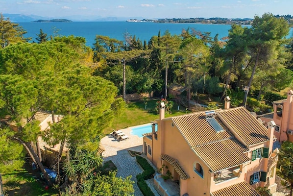 Une villa de style méditerranéen dotée d’une piscine, entourée d’une végétation luxuriante et offrant une vue sur une mer calme.