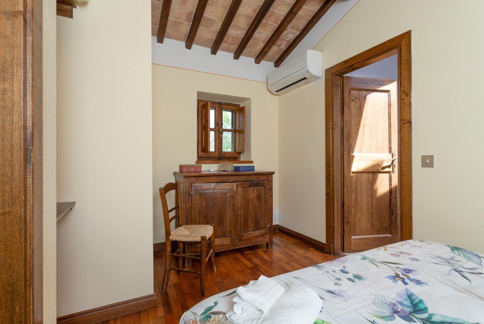 A bedroom with a wooden bed, a desk with a chair, a window, and an air conditioning unit.