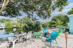 An outdoor seating area with a table and chairs, a small pond, and trees in the background.