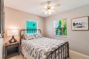 A bedroom with a bed, a nightstand, a ceiling fan, and two windows with blinds.