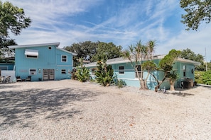 A two-story building with a light blue exterior, a gravel driveway, and surrounding greenery.