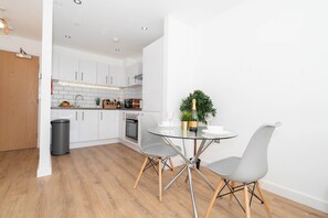 A modern kitchen with white cabinets, a stainless steel oven, and a glass dining table with two chairs.