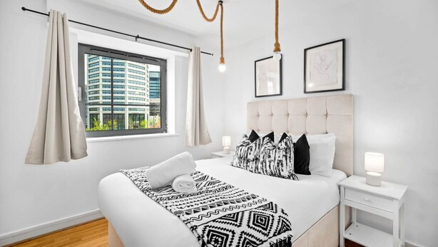 Habitación de hotel moderna con una cama grande, una mesita de noche con lámpara y vista a un edificio a través de la ventana.