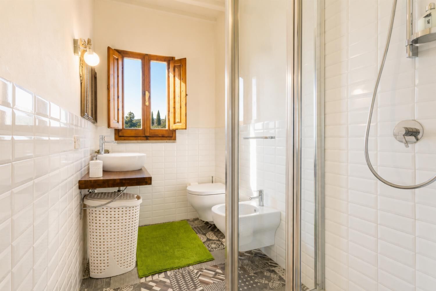 A bathroom with a shower, toilet, sink, and a window with wooden shutters.