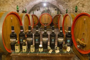 A wine cellar with rows of wooden barrels and bottles of wine.