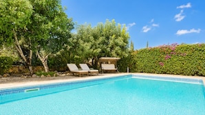 A clear blue pool with lounge chairs and a stone wall.