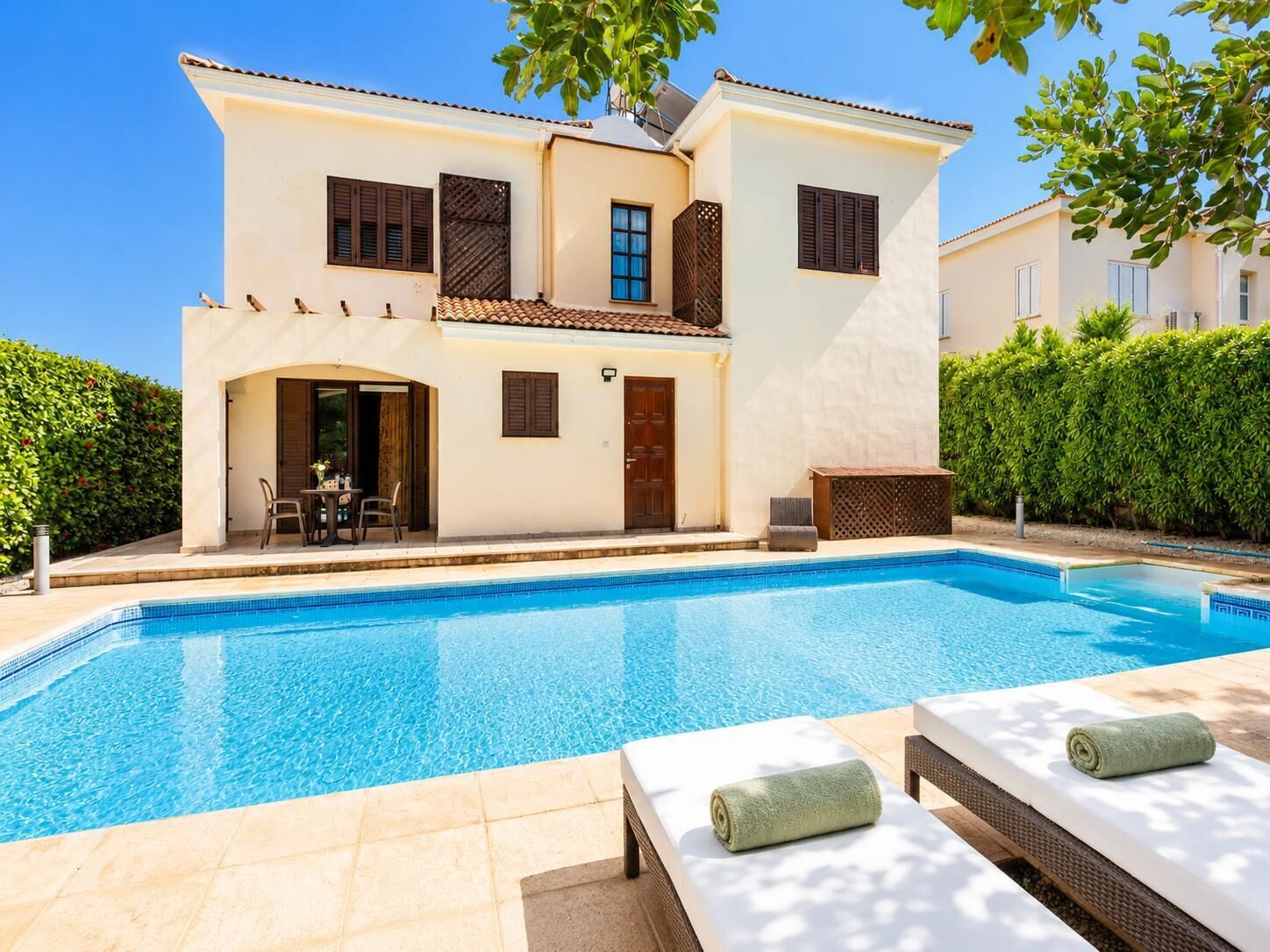 Una casa de dos pisos con piscina, mobiliario exterior y un jardín cuidado.