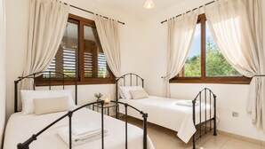 A bedroom with two beds, each with a metal frame, and a window with curtains.