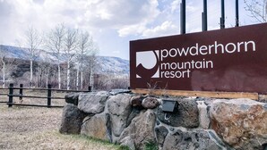 Señal de Powderhorn Mountain Resort con un muro de piedra y vistas a montañas y árboles.