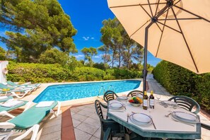 Un área de comedor junto a la piscina con una mesa para dos, una piscina y una sombrilla grande.