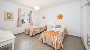 Une chambre avec deux lits, une fenêtre avec des rideaux, une table de chevet avec une lampe et une armoire.