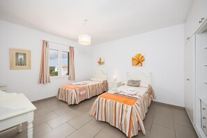 Un dormitorio con dos camas, una ventana con cortinas, una mesita de noche con lámpara y un armario.