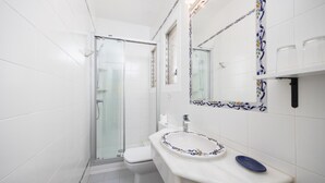 Une salle de bain dotée d’une douche à parois de verre, de toilettes, d’un lavabo avec un récipient décoratif et d’un miroir orné d’une bordure de motifs floraux en carreaux.