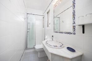 Een badkamer met een douchecabine van glas, een toilet, een wastafel met decoratieve wasbak en een spiegel met een bloemrijk tegelomlijsting.