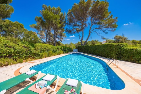 Una piscina con sillones de descanso y un cielo azul despejado.