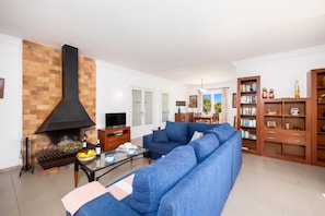 A living room with a brick fireplace, a blue sofa, a glass coffee table, and a bookshelf.