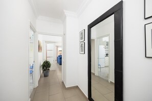 Un pasillo con una planta en maceta, un sofá azul y una cocina visible a través de una puerta abierta.