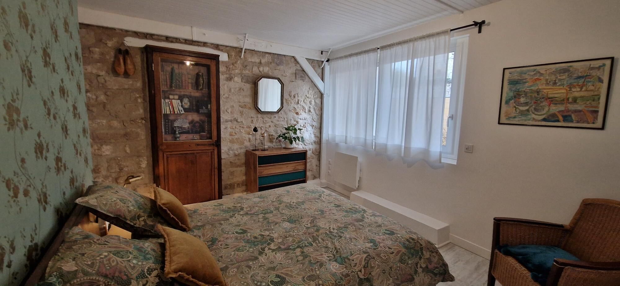 A bedroom with a bed, a dresser, a chair, a mirror, and a window with curtains.