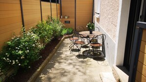 A small outdoor patio with a table and chairs, surrounded by a low brick wall and a variety of plants.