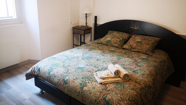 A neatly made bed with a patterned bedspread, a small bedside table with a lamp, and a window with blinds.