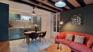 A modern living space with a dining area, a sofa, and a kitchen in the background.
