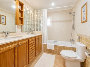 A bathroom with wooden cabinets, a double sink, a bathtub, and a toilet.