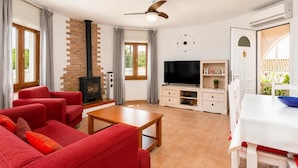 A living room with a fireplace, a TV, a dining area, and a view of greenery outside.