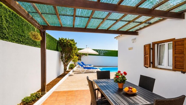 A covered outdoor area with a pool, lounge chairs, and a table with a fruit bowl.
