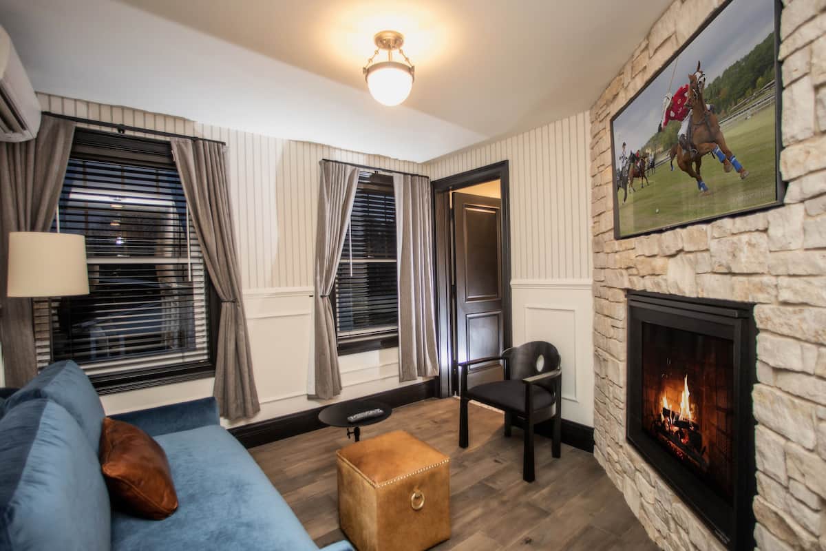A living room with a stone fireplace, a blue sofa, a leather chair, and a brown ottoman.