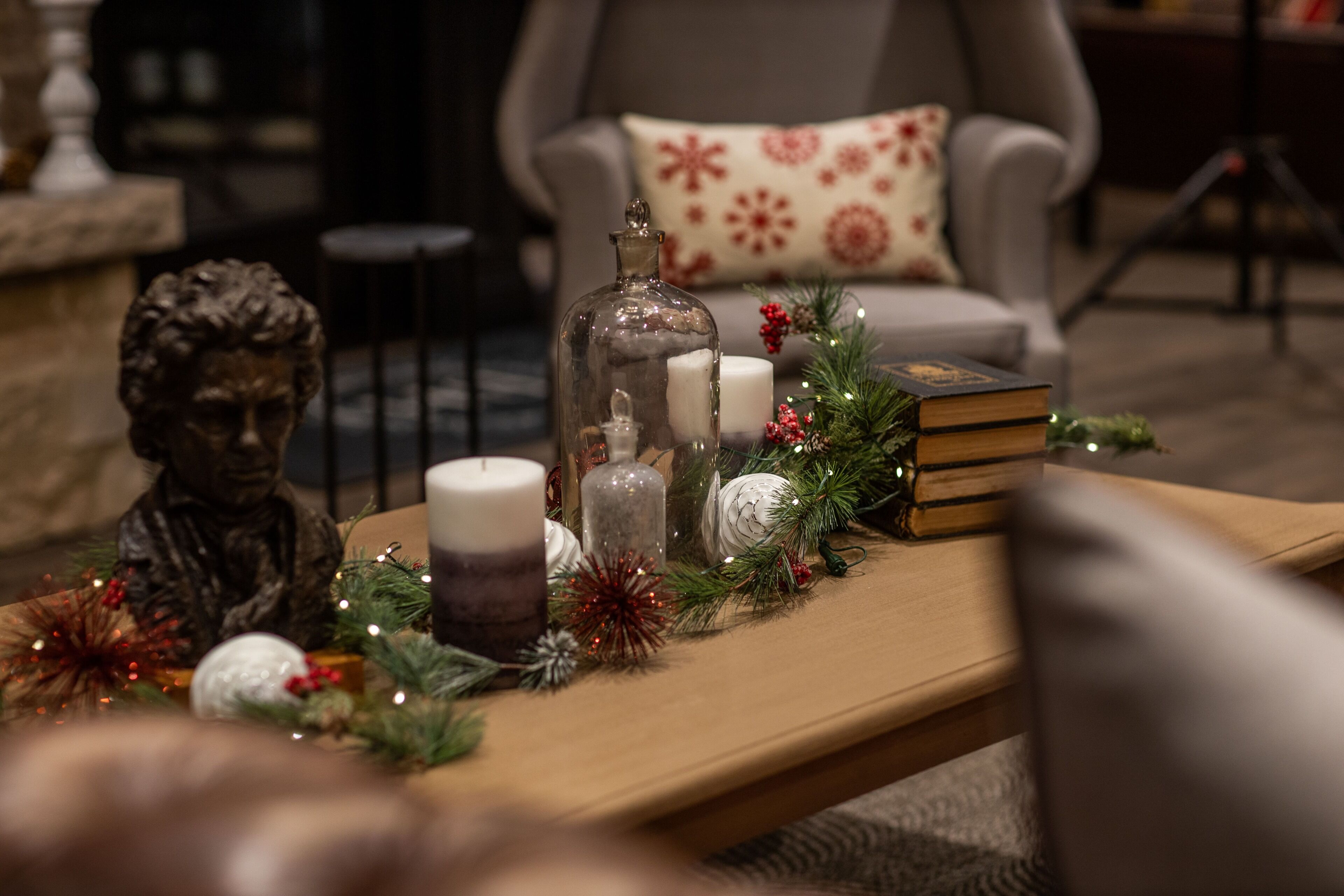 A cozy living room with a wooden coffee table adorned with Christmas decorations, including candles, a glass jar, and a statue.