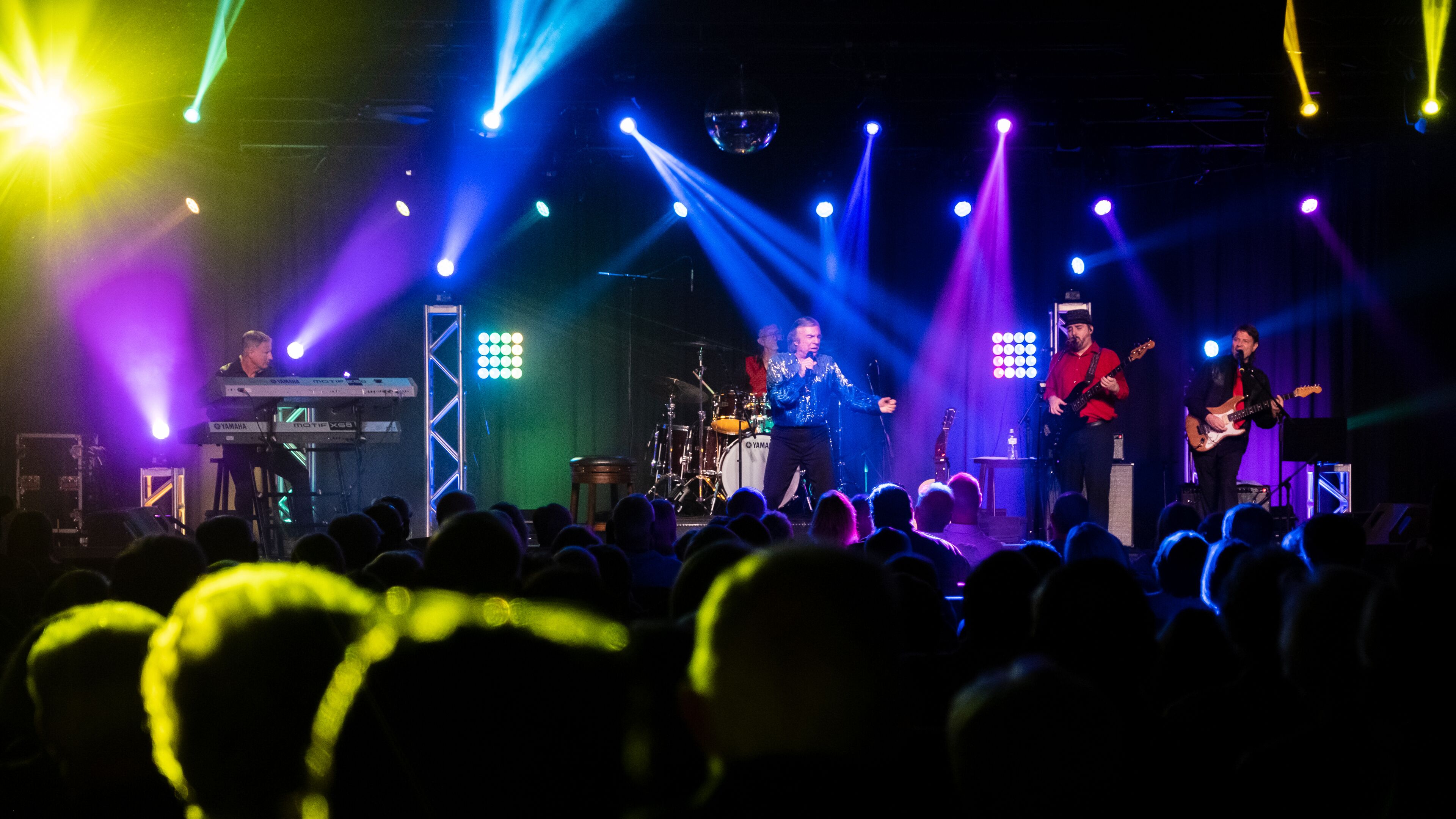 A band performing on a stage with a keyboard, drums, and guitars.