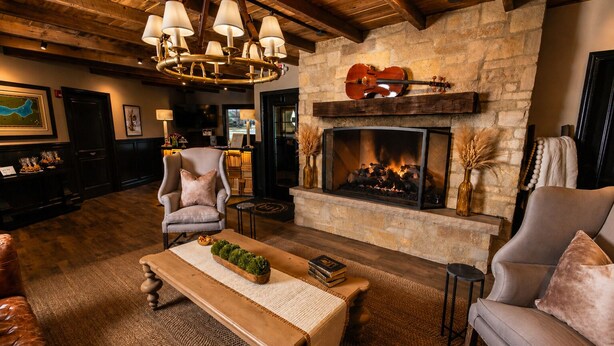 A cozy living room with a stone fireplace, a chandelier, and comfortable seating. - The Belfry House (Williams Bay)