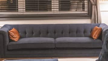 A dark grey sofa with two brown cushions, positioned in front of a window with blinds.