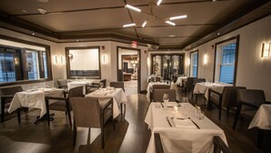 A restaurant with multiple tables set for dining, featuring a modern interior with wooden flooring and white tablecloths. - The Belfry House (Williams Bay)