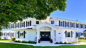 A two-story white house with a dark front door, a covered porch, and a well-maintained lawn. - The Belfry House (Williams Bay)