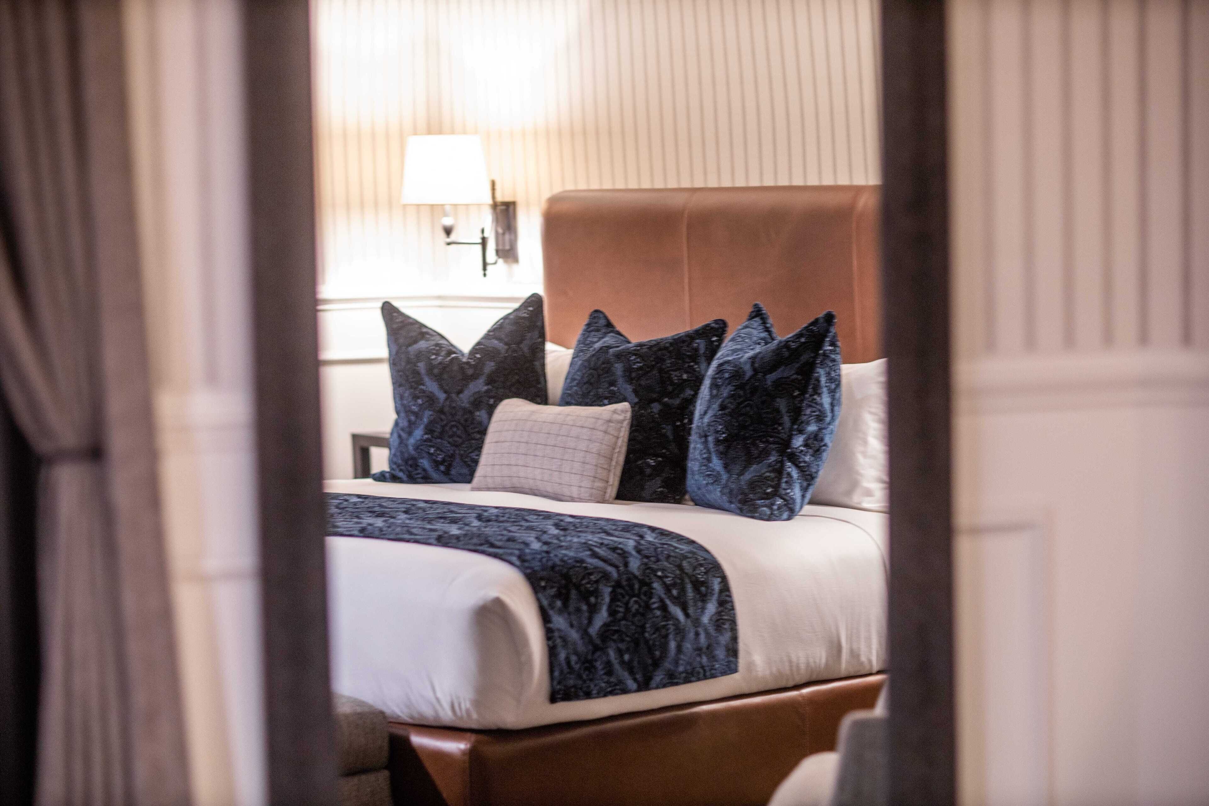 A neatly made bed with a patterned bedspread and multiple pillows, a wooden headboard, and a lamp on a bedside table.