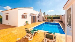 A white villa with a swimming pool, two lounge chairs, and a patio area.