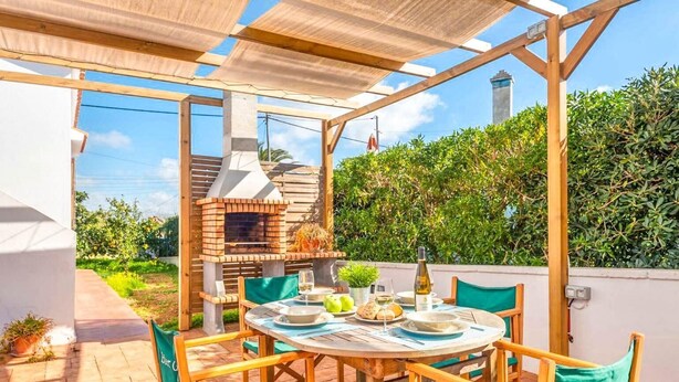 An outdoor patio with a brick oven, wooden table, and chairs.