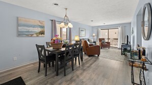 A spacious living room with a dining area, a large mirror, and a view to the outside. - Shipwatch Pointe I F117 Two Bedroom Condo First Floor Condo (Myrtle Beach)
