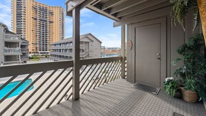 A balcony with a view of a tall hotel building, a pool, and a door with a doormat. - Shipwatch Pointe I F117 Two Bedroom Condo First Floor Condo (Myrtle Beach)