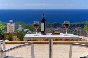 Ein Tisch mit einer Weinflasche und zwei Gläsern auf einer Terrasse mit Meerblick.
